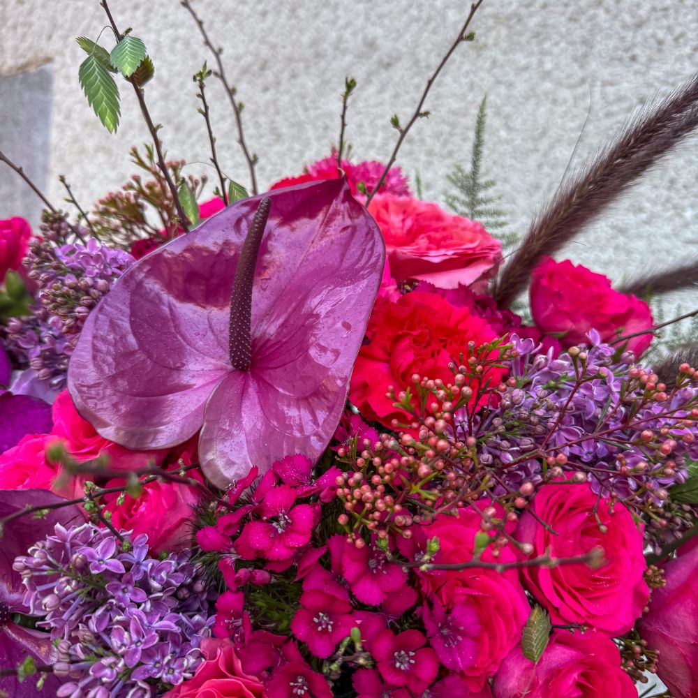 Detaljbild på festlig bukett med anthurium, rosor och nejlikor i rosa och lila nyanser