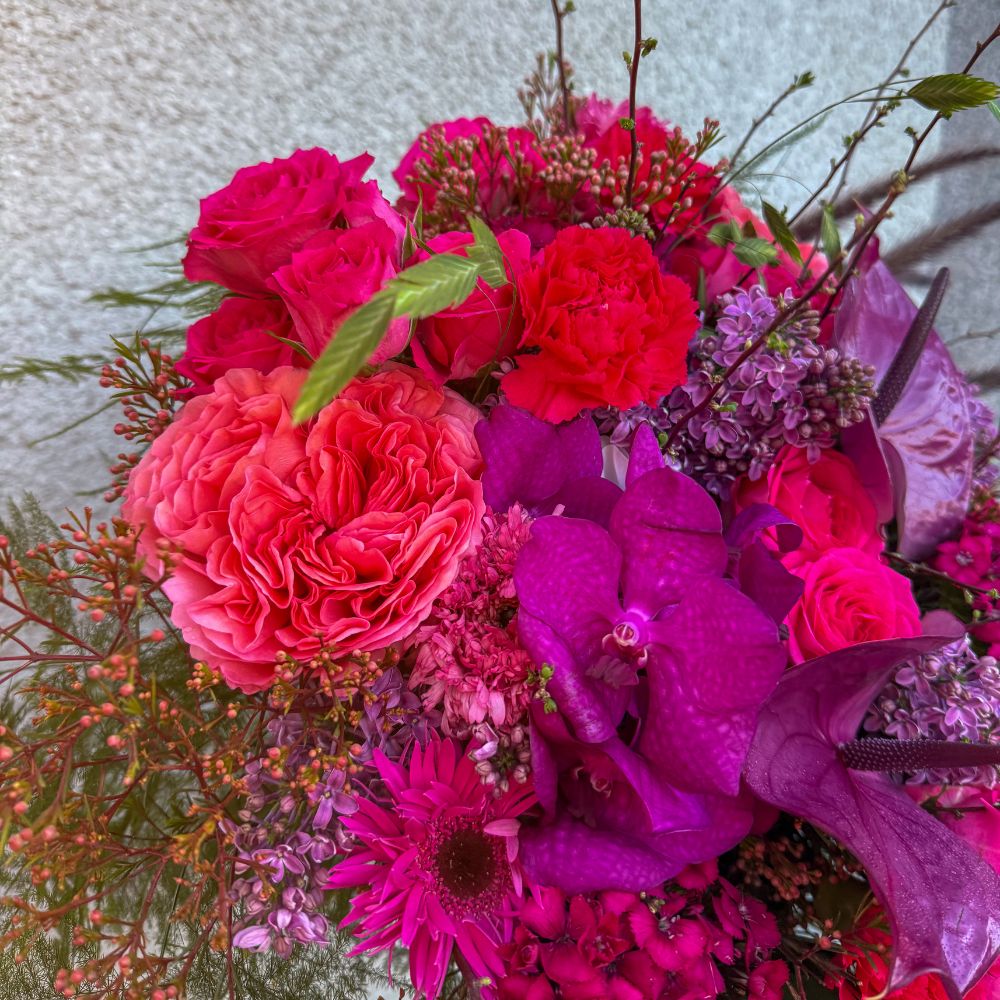 Närbild på vinnarbuketten med lila orkidéer, eleganta rosor och färgglada nejlikor, skapad av Interflora Sundbybergs Blomsterhandel
