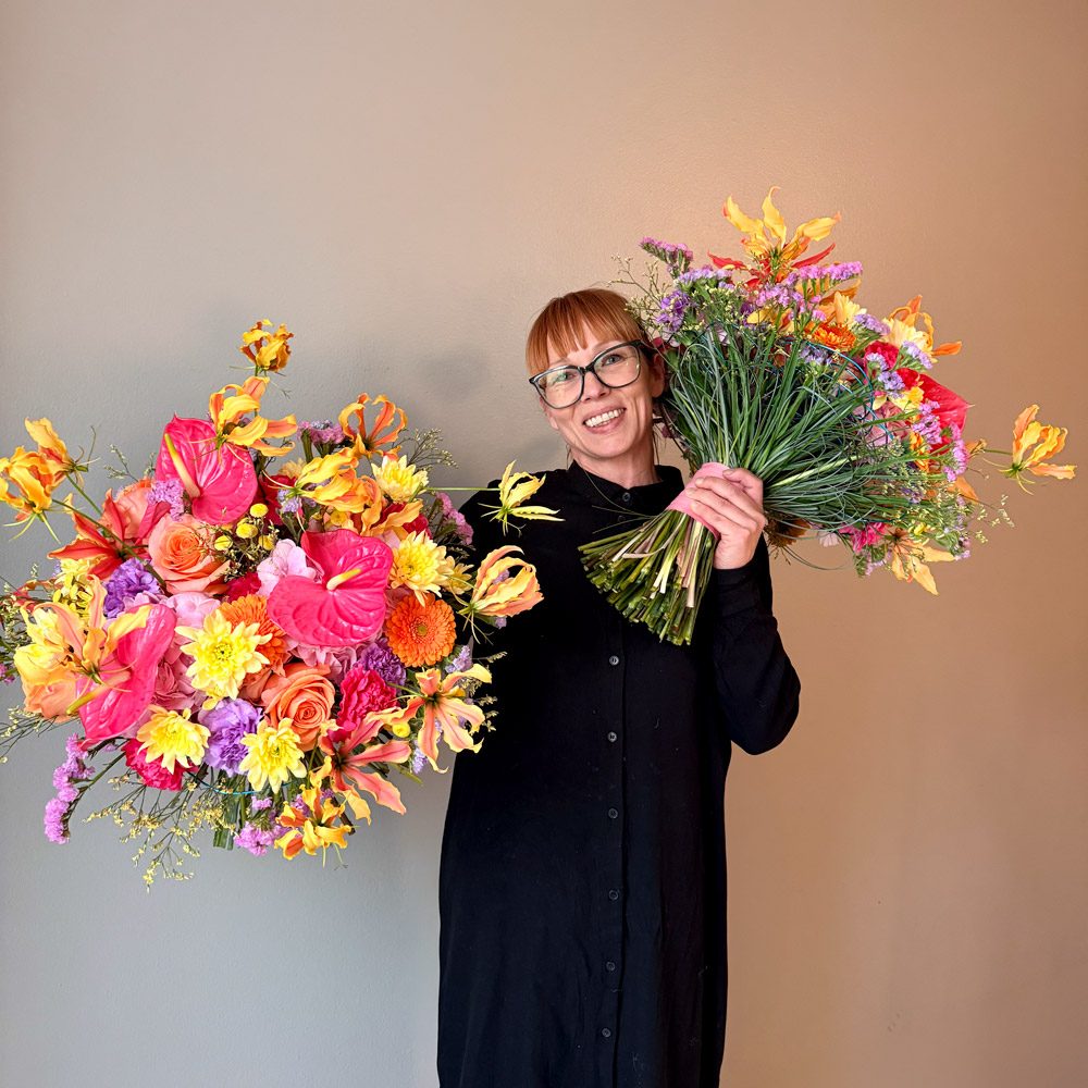 Leende florist från Interflora Qvist & Lina håller två färgsprakande vinnarbuketter i händerna