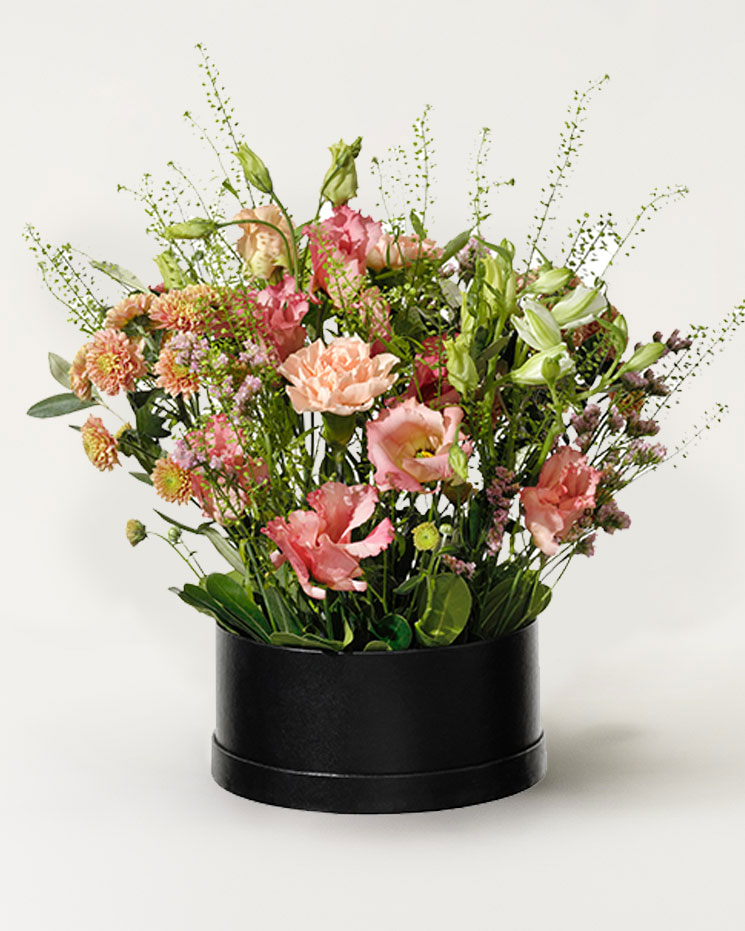 Rund box (som en liten hattask), fylld med blommor i rosa och aprikosa nejlikor, prärieklockor och santini. Superfin, finns hos Interflora!