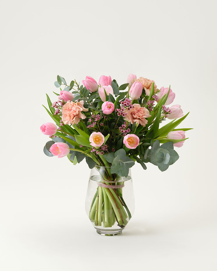 Hos Interflora: fin blombukett med rosa tulpaner och vaxblommor tillsammans med aprikosa nejlikor, eucalyptus och dekorationsgrönt.